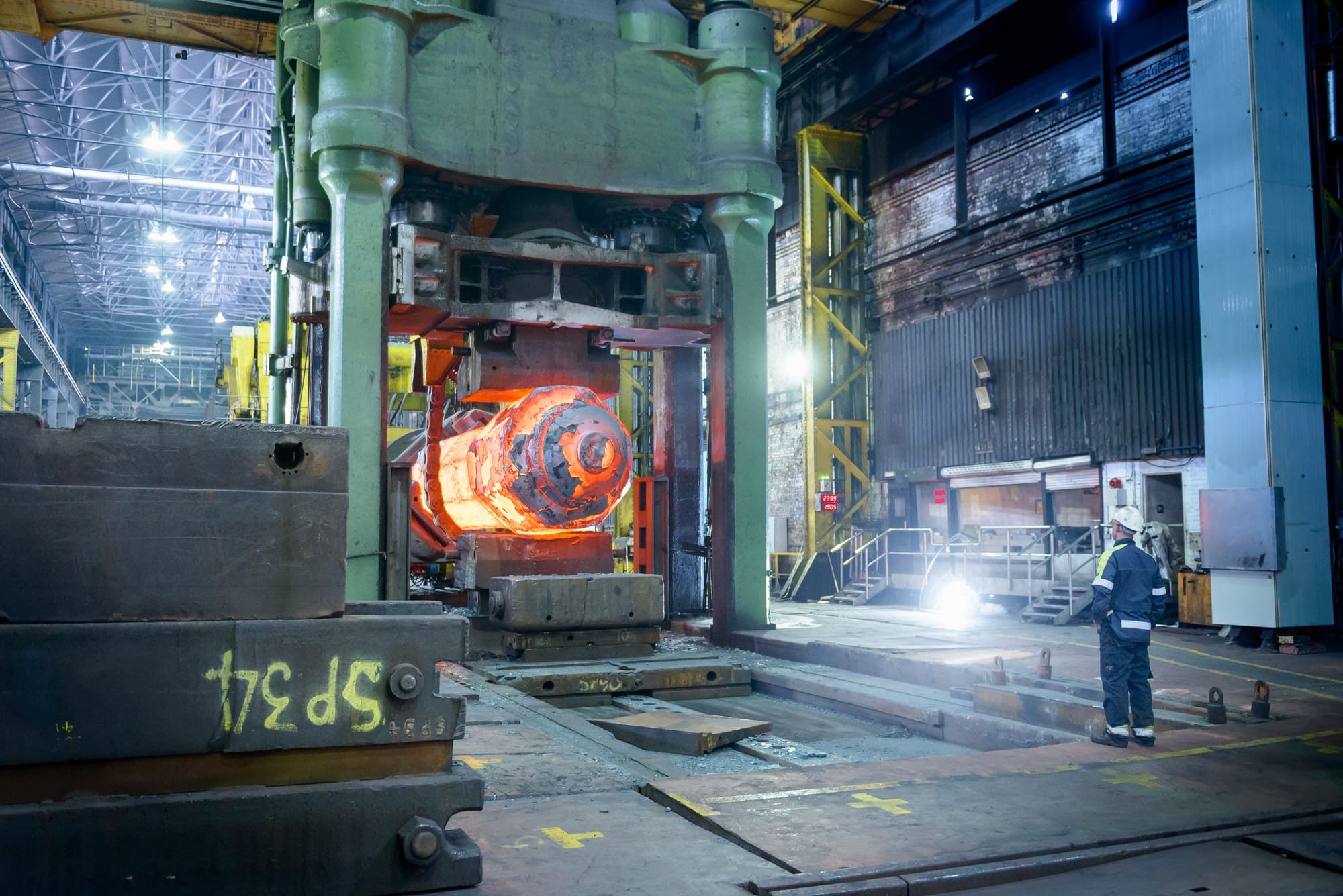 Steelworker inspects hot steel in forging press in steelworks